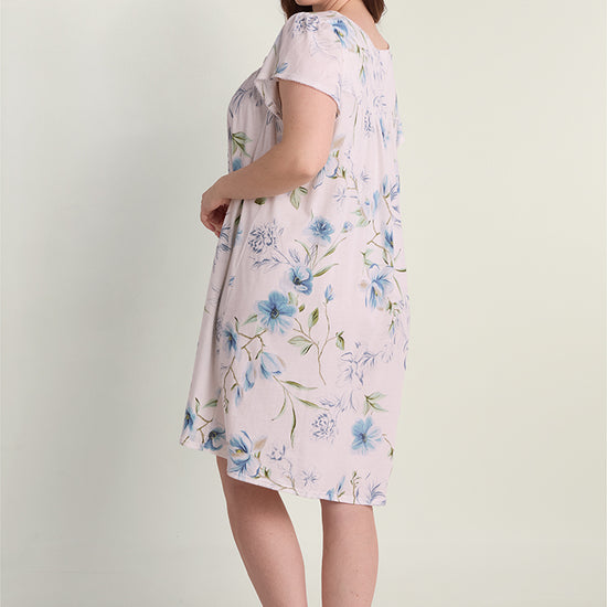 Woman wearing a light pink short nightgown with blue floral print, shown from the back in a three-quarter view.