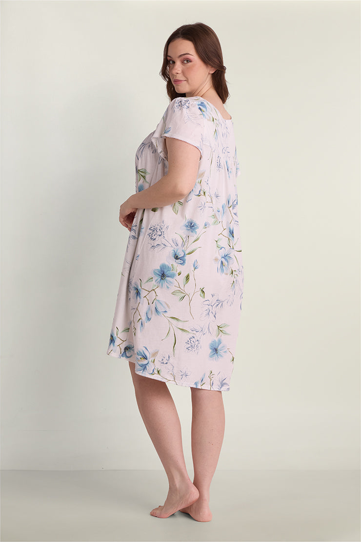 Woman wearing a light pink short nightgown with blue floral print, shown from the back in a three-quarter view.