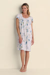 Woman wearing a lavender floral short nightgown with blue flowers, standing against a cream background.