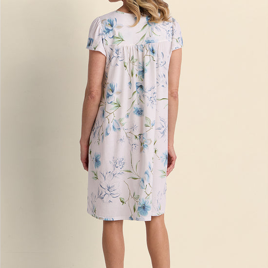 Woman wearing lavender floral short-sleeve nightgown, shown from back view against neutral background.