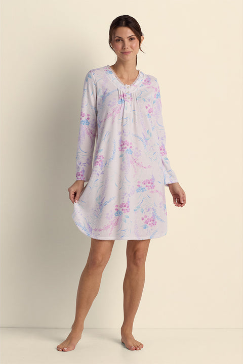 Woman wearing a lavender floral short nightgown with long sleeves, standing against a neutral background.