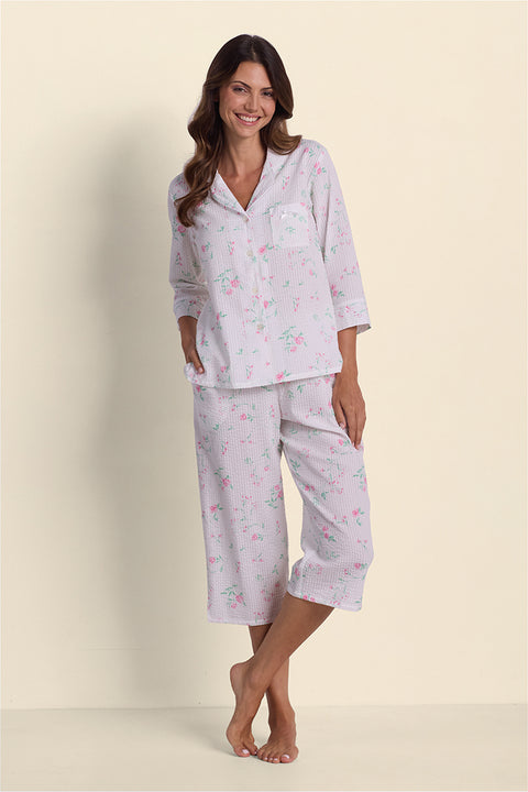 Woman wearing lavender seersucker pajama set with pink floral print, three-quarter sleeves, cropped pants, standing barefoot.