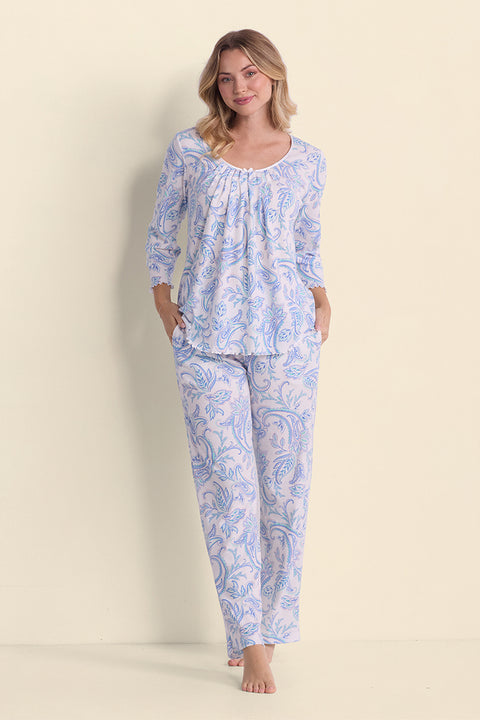 Woman wearing blue paisley print cotton pajama set with three-quarter sleeves, standing against cream background.