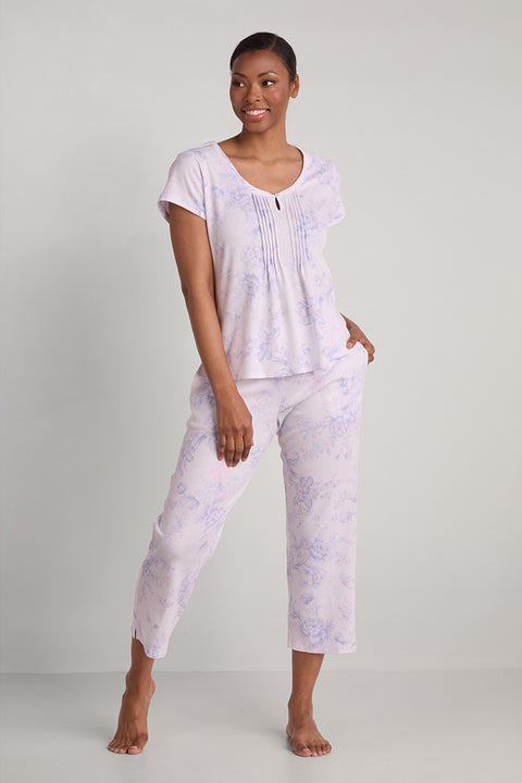 Woman wearing lavender tie-dye short-sleeve pajama top and cropped pants, standing against white background.