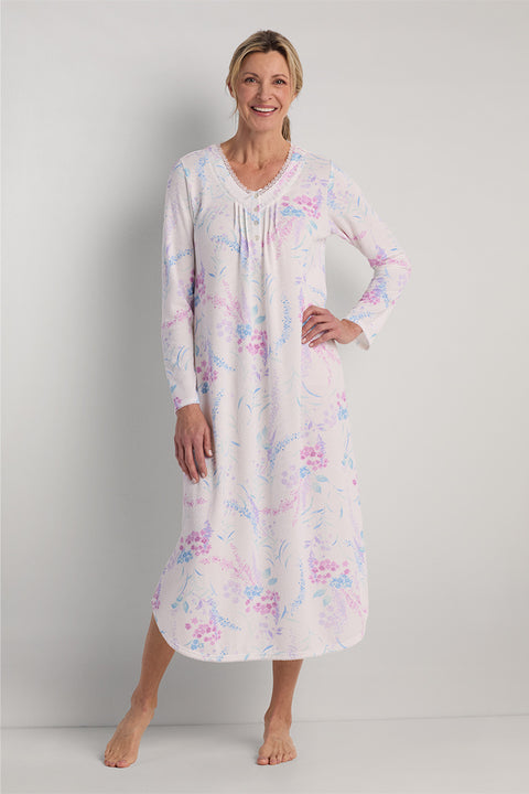 Woman wearing a long nightgown with pink and blue floral print on white background, long sleeves, V-neckline.