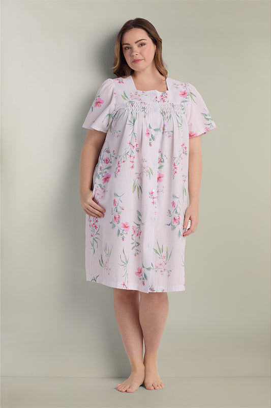 Woman wearing a lavender seersucker short robe with pink floral print and flutter sleeves, standing against a neutral