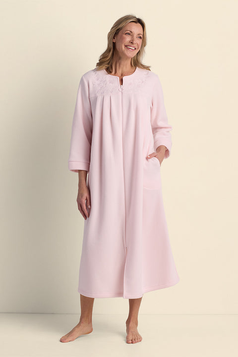 Woman wearing a pink fleece long robe with three-quarter sleeves and front zip closure, standing against a neutral