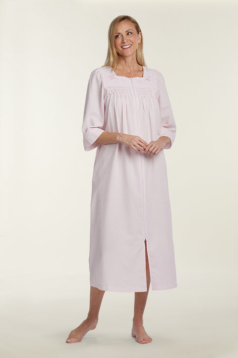 Woman wearing a light pink seersucker long robe with three-quarter sleeves and front slit, standing against a neutral