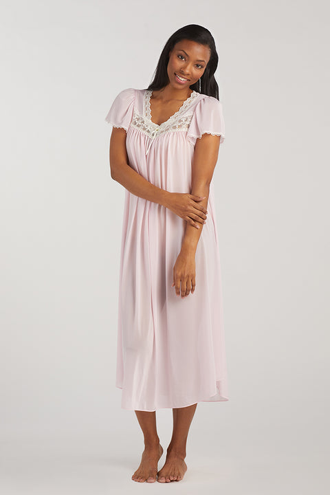 Woman wearing a pink short-sleeved long nightgown with lace neckline, standing against white background.